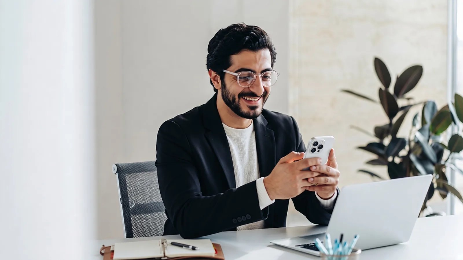 Sultan Rashid Abdullah Al Shene, Founder of Al Shene Marine Holding, smiling at his phone at his office desk with a laptop and notebook
